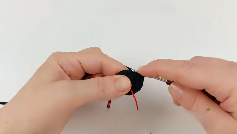 Black amigurumi ball R3 increase round, red yarn tail visible.
