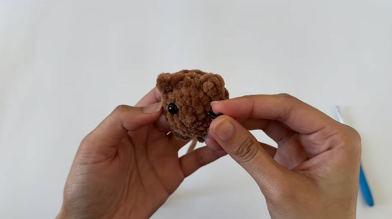 Black safety eye being inserted into the brown fluffy kitten head.