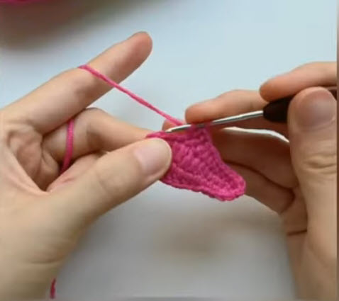 Completed pink crochet petal, hook working the edge stitch.