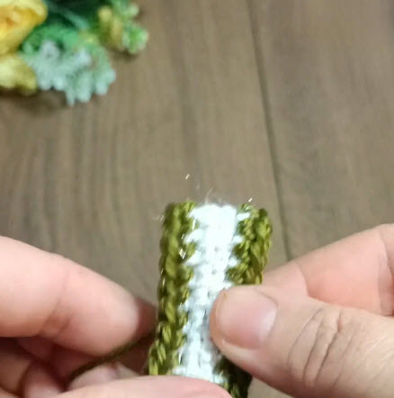 Green and white crochet piece held between fingers.