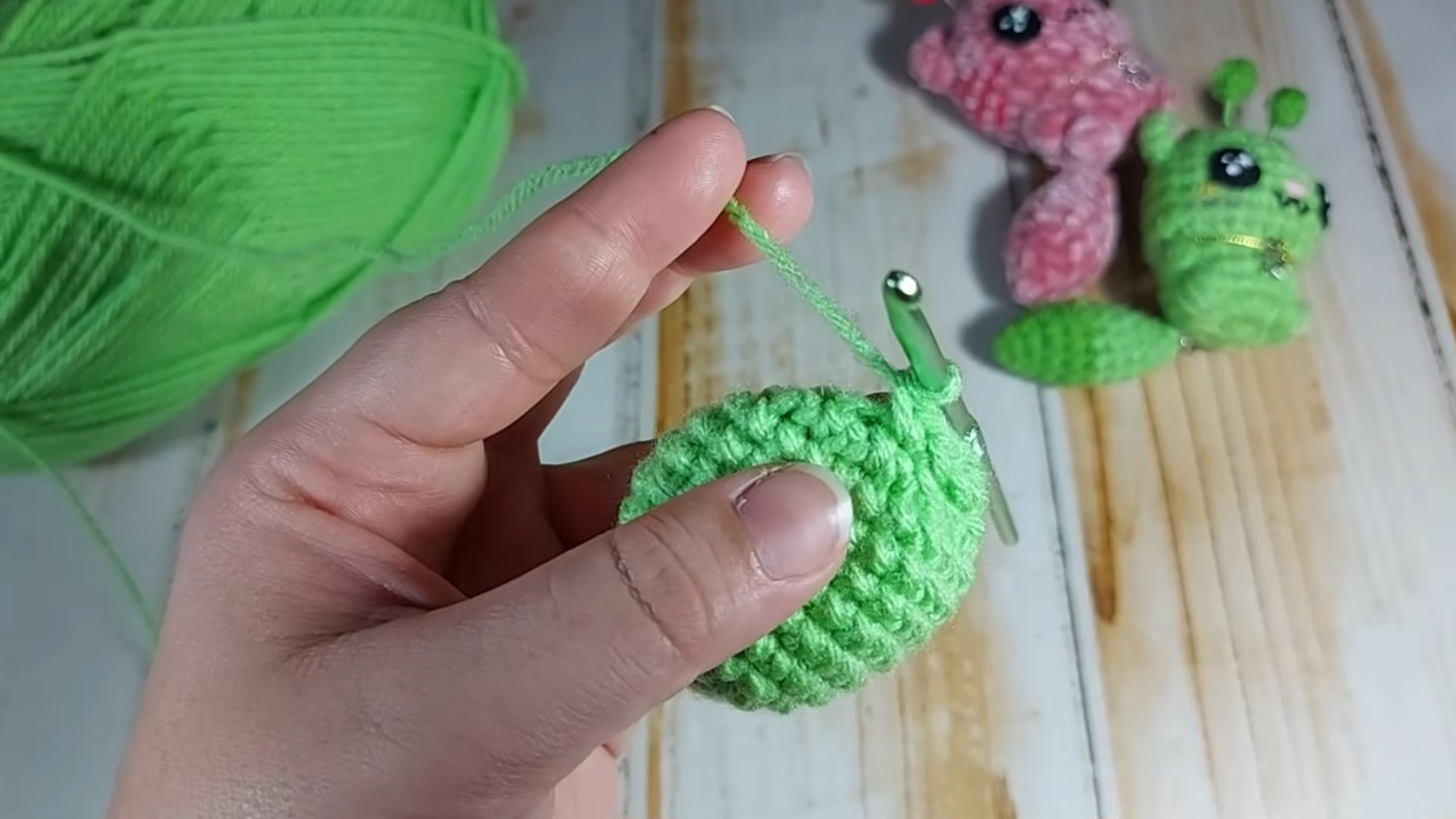 Holding completed green crocheted ball with hook inside