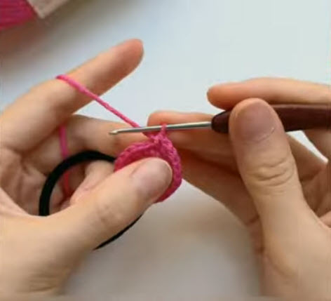 Pink flower petal being crocheted onto a black hair tie.