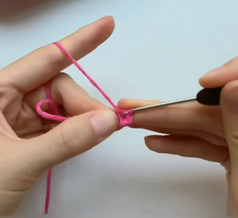 Pink yarn loop being tightened with finger and hook.