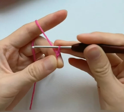 Pink yarn slip knot being made on the crochet hook.