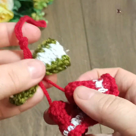 Red and green crochet bell pieces being joined together with red thread.