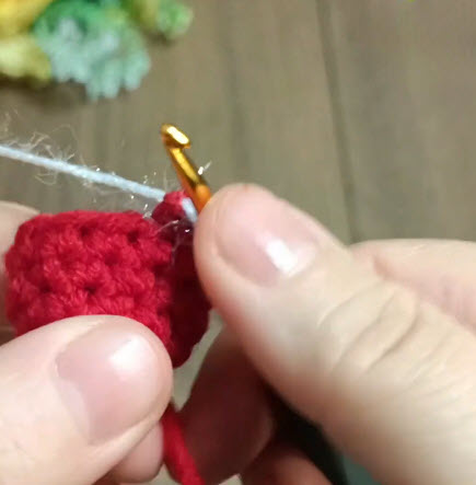 Red crochet bell shape being stitched with white sparkly thread.