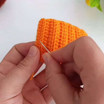 Ribbed orange crochet panel being seamed with a yarn needle