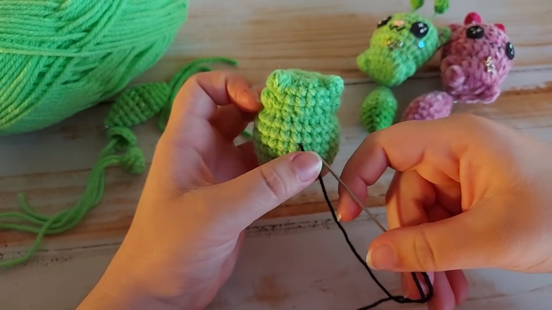 Sewing black thread detail onto green crocheted piece
