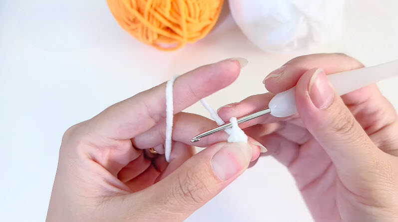 White magic ring mein 6sc, crochet hook aur orange-white yarn balls.