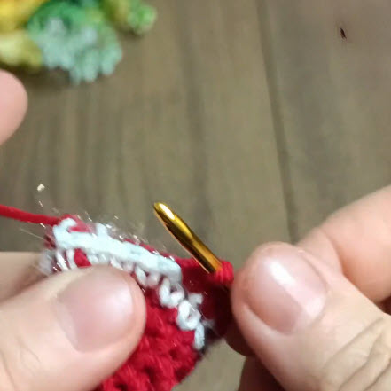 White sparkly thread being crocheted onto the red bell edge.