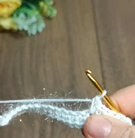 White sparkly yarn edge stitch being worked with the hook.