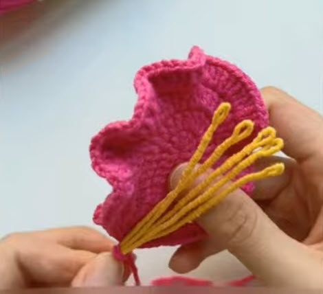 Yellow yarn stamens being attached inside the pink crochet flower.