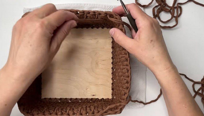 Crochet makeup basket sides rising from the wooden bottom with the hook above.