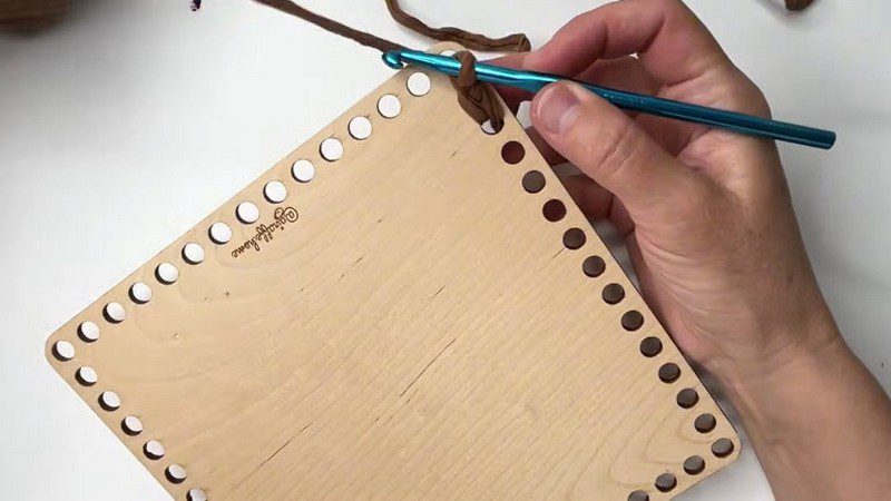 Brown fabric yarn started through the holes of a wooden base.