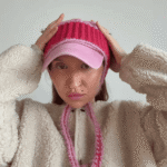 Pink baseball cap upcycled with a hot pink ribbed crochet crown and long pink braided ear ties, worn with a cream fleece jacket