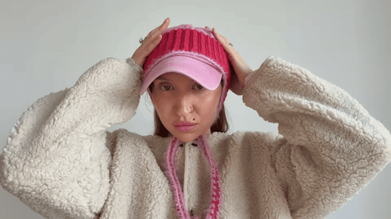 Pink baseball cap upcycled with a hot pink ribbed crochet crown and long pink braided ear ties, worn with a cream fleece jacket