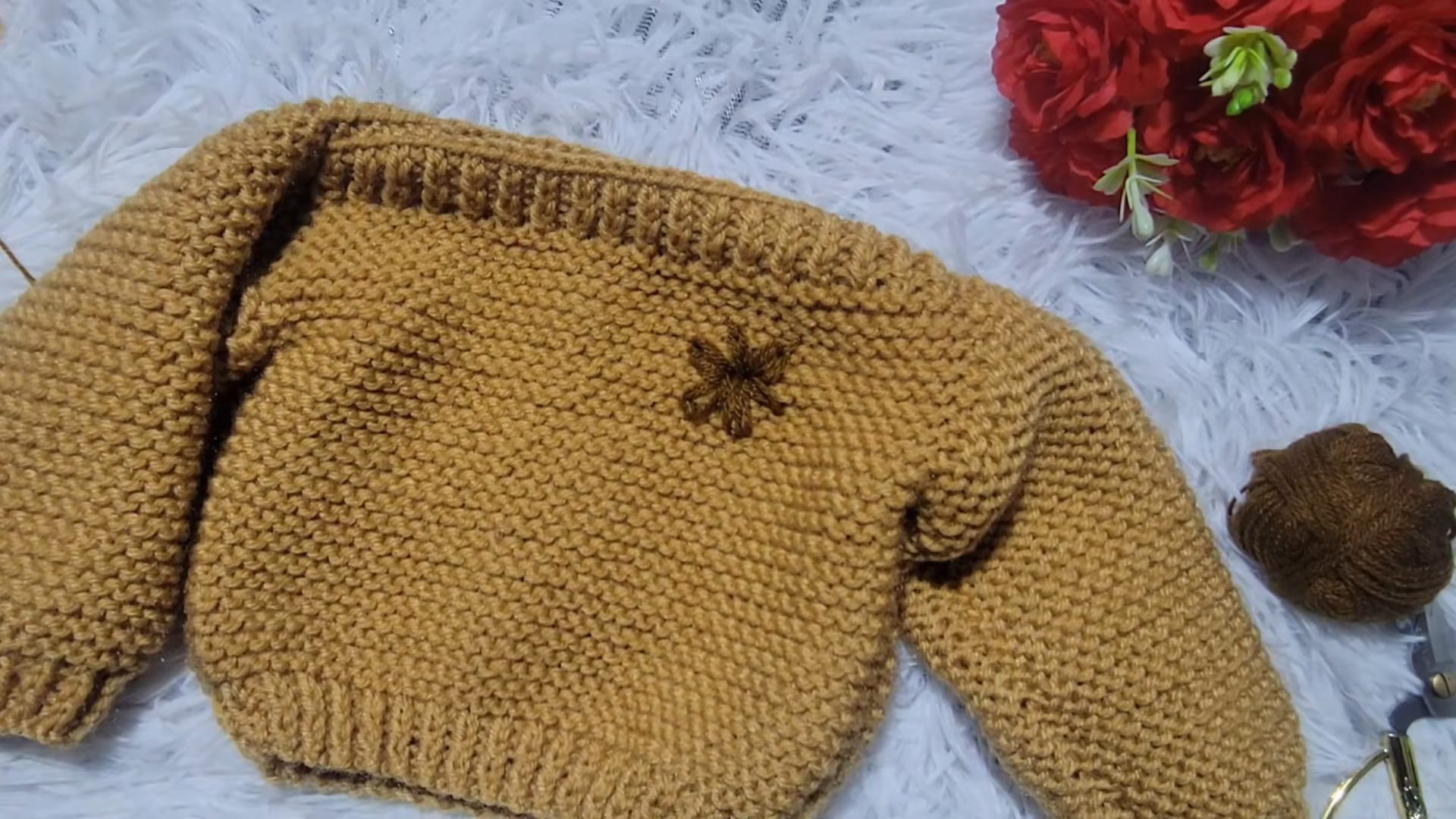 Finished mustard baby sweater with a small embroidered flower.