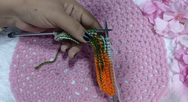 Knitting a striped strip in green, orange and white.