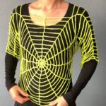 Neon yellow crochet spider web top worn over a black long sleeve shirt, with radiating web lines and a center spiral
