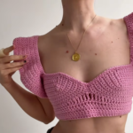 Pink crochet sweetheart neckline crop top with flutter ruffle sleeves and a small openwork detail at the center, worn with a gold pendant necklace