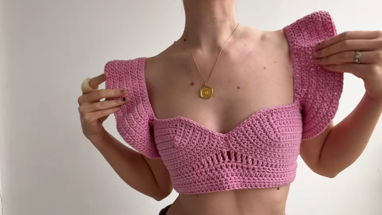Pink crochet sweetheart neckline crop top with flutter ruffle sleeves and a small openwork detail at the center, worn with a gold pendant necklace