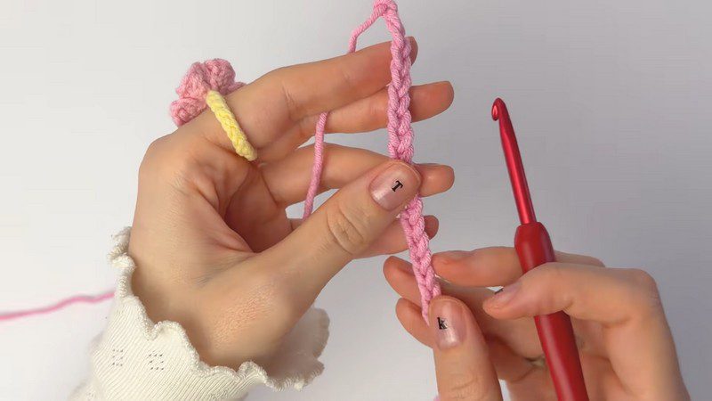 Pink yarn starting chain held beside a red crochet hook.