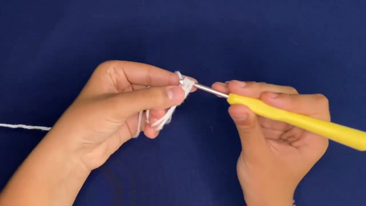 Starting a white yarn base with the hook held in both hands for the crochet Coraline sweater