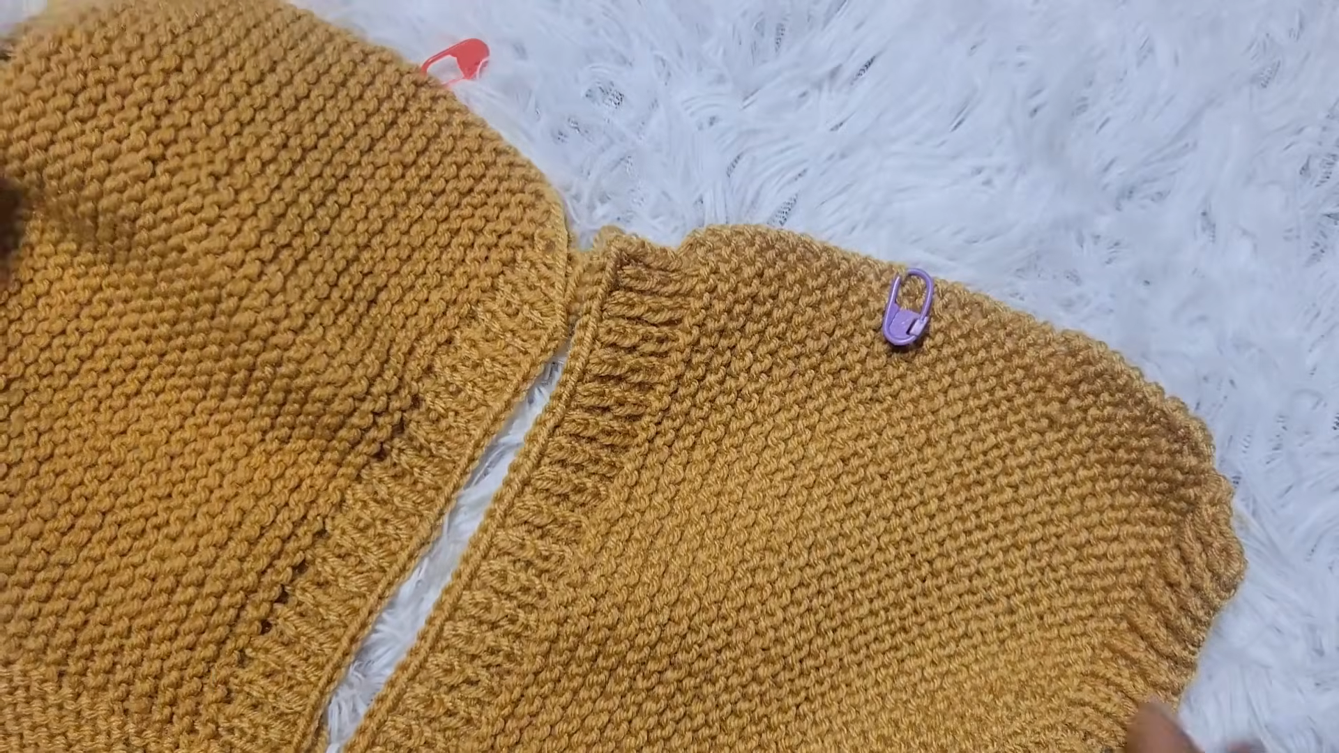Two mustard sweater panels with red and purple stitch markers.