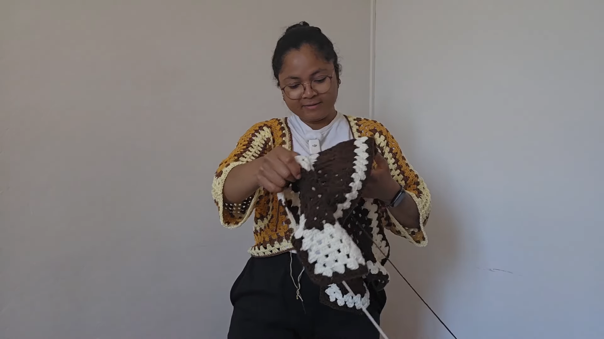 Woman wearing the granny cardigan while holding a brown and white square.