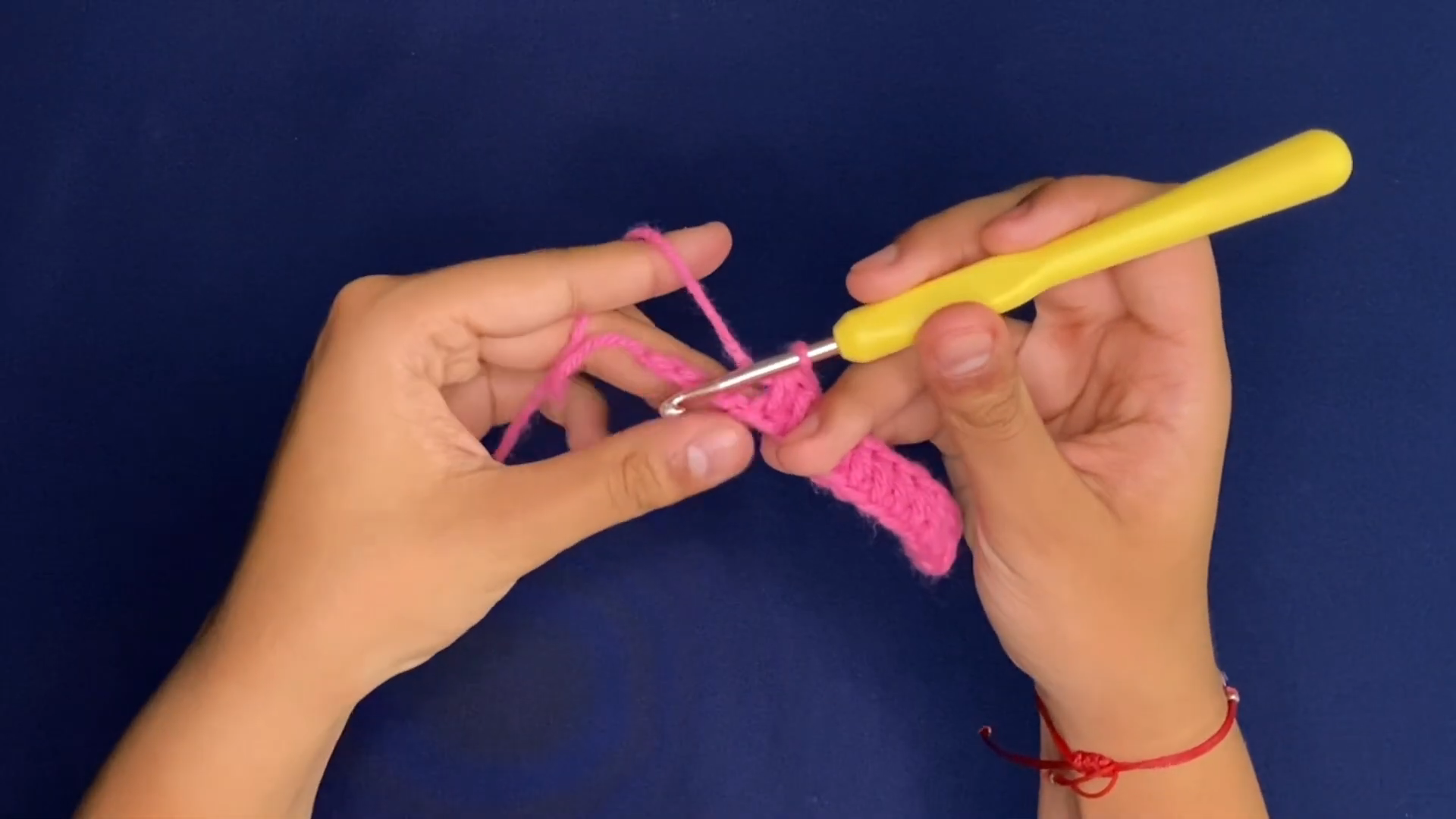 Working a narrow pink strip with a yellow hook for the crochet Coraline sweater